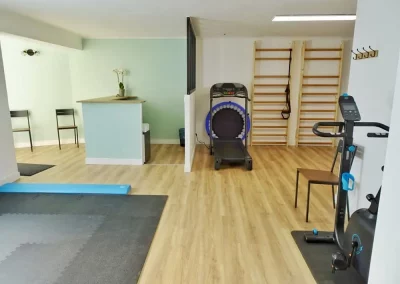 Un cabinet de kinésithérapeute avec une banque d'accueil, un tapis de course et un vélo d'intérieur