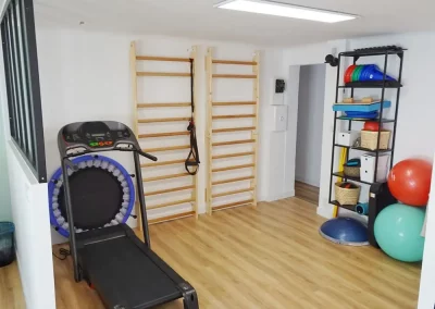 Un cabinet de kinésithérapie avec un tapis de course, un trampoline et des ballons de gym